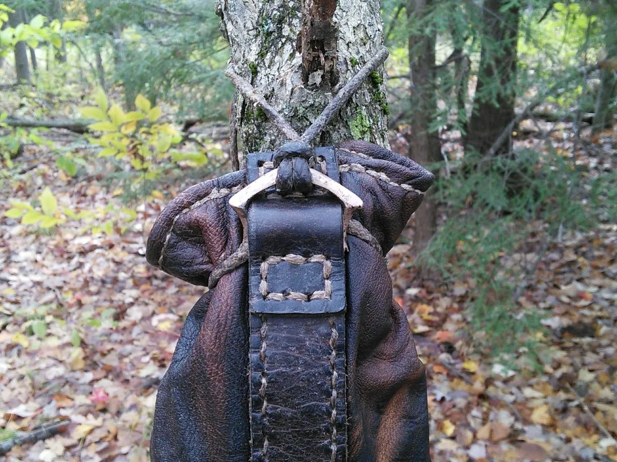 A dark leather snapsack with a cast buckle, hanging in autumn woods